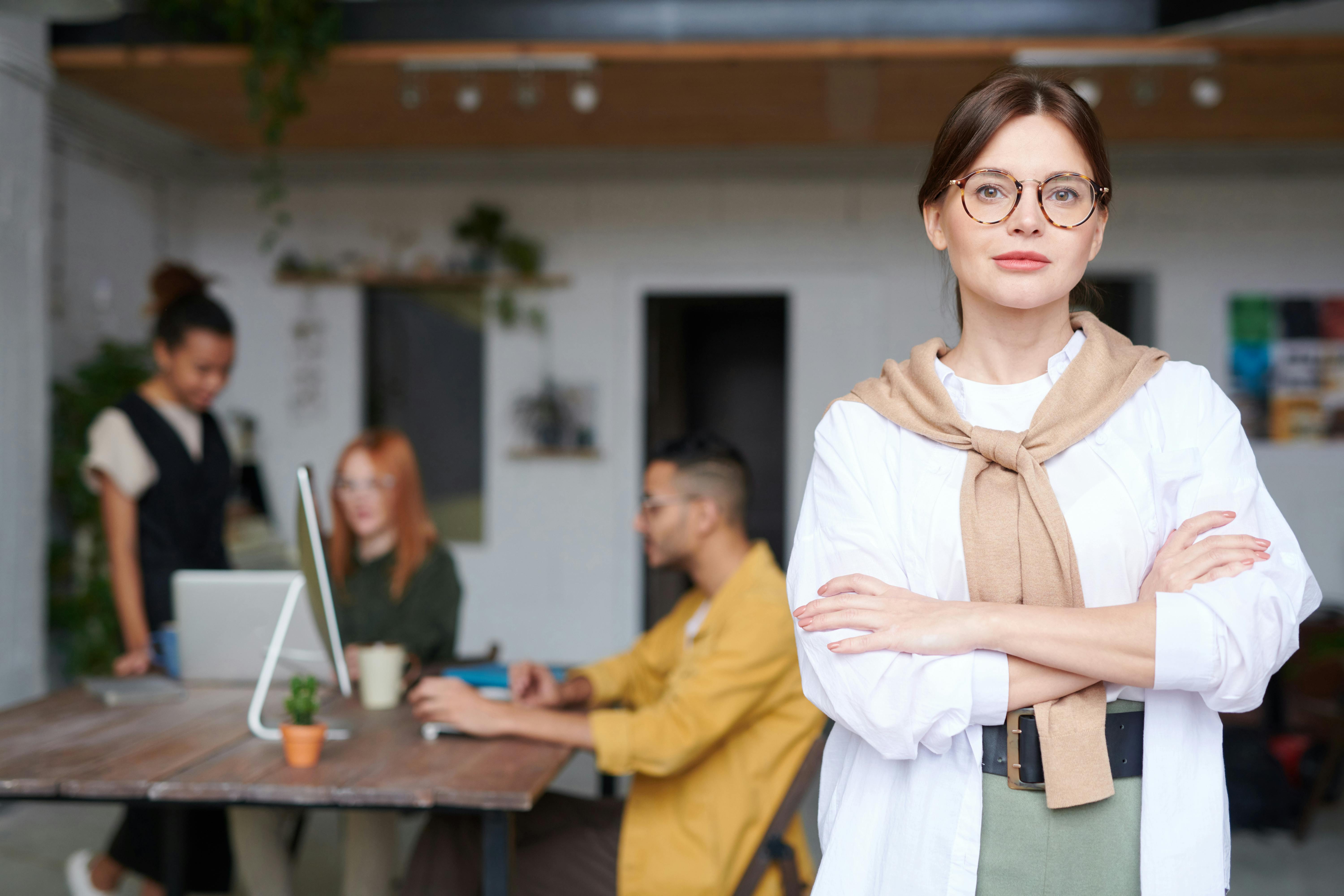 A woman in professional clothing with group of people working in an office in the background